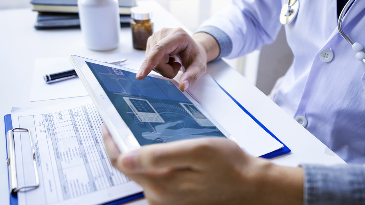 Doctor seated at a desk working on a tablet showing patient diagnostics.