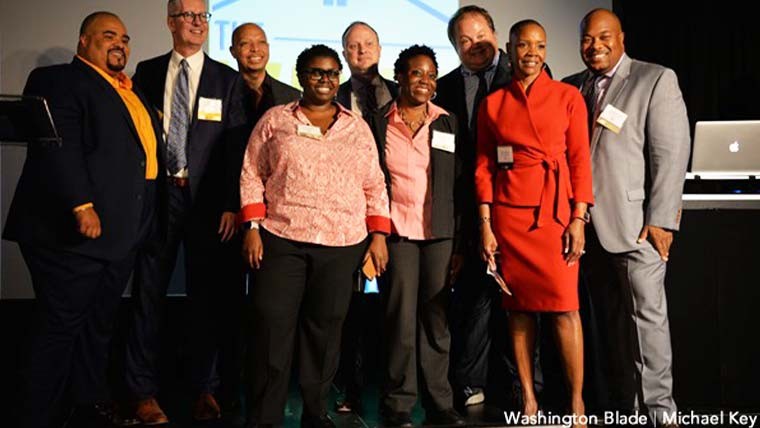 Photo of Sian and other individuals standing on stage smiling with a projector screen behind them.