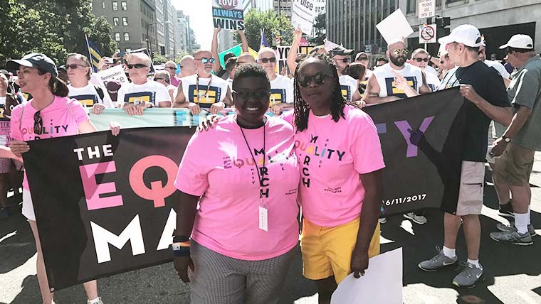 Sian outside on the street with a friend at a march in from of a banner and other march participants