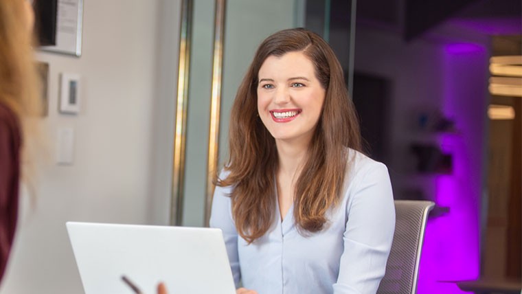 Woman sitting and smiling with a laptop in front of her.