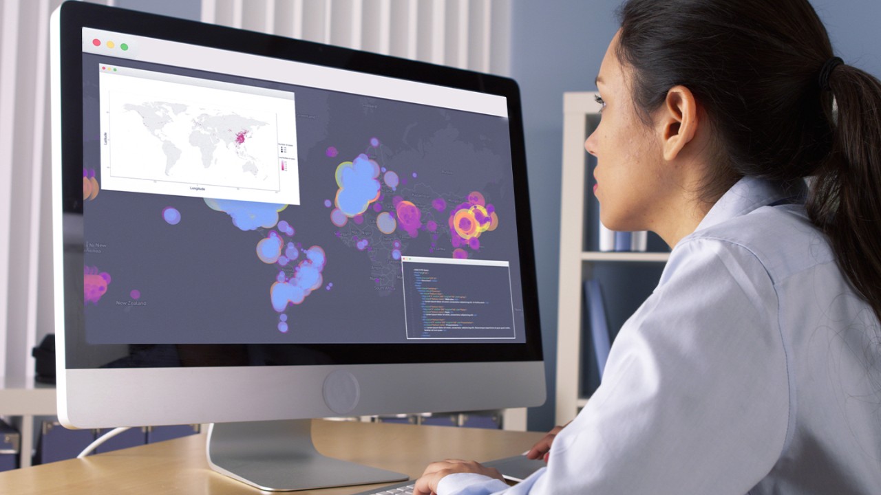 Woman sitting at desk looking at a map of the world on a desktop monitor.