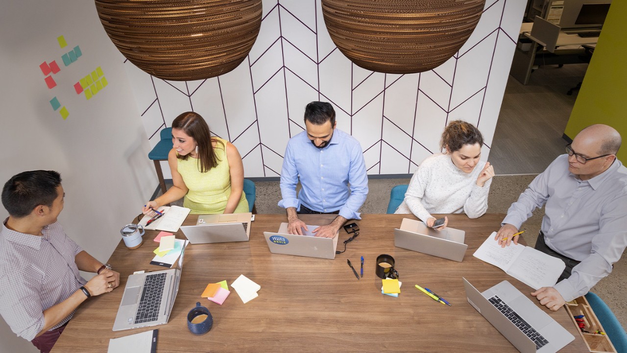 Group of men and women discussing ideas around a table with laptops