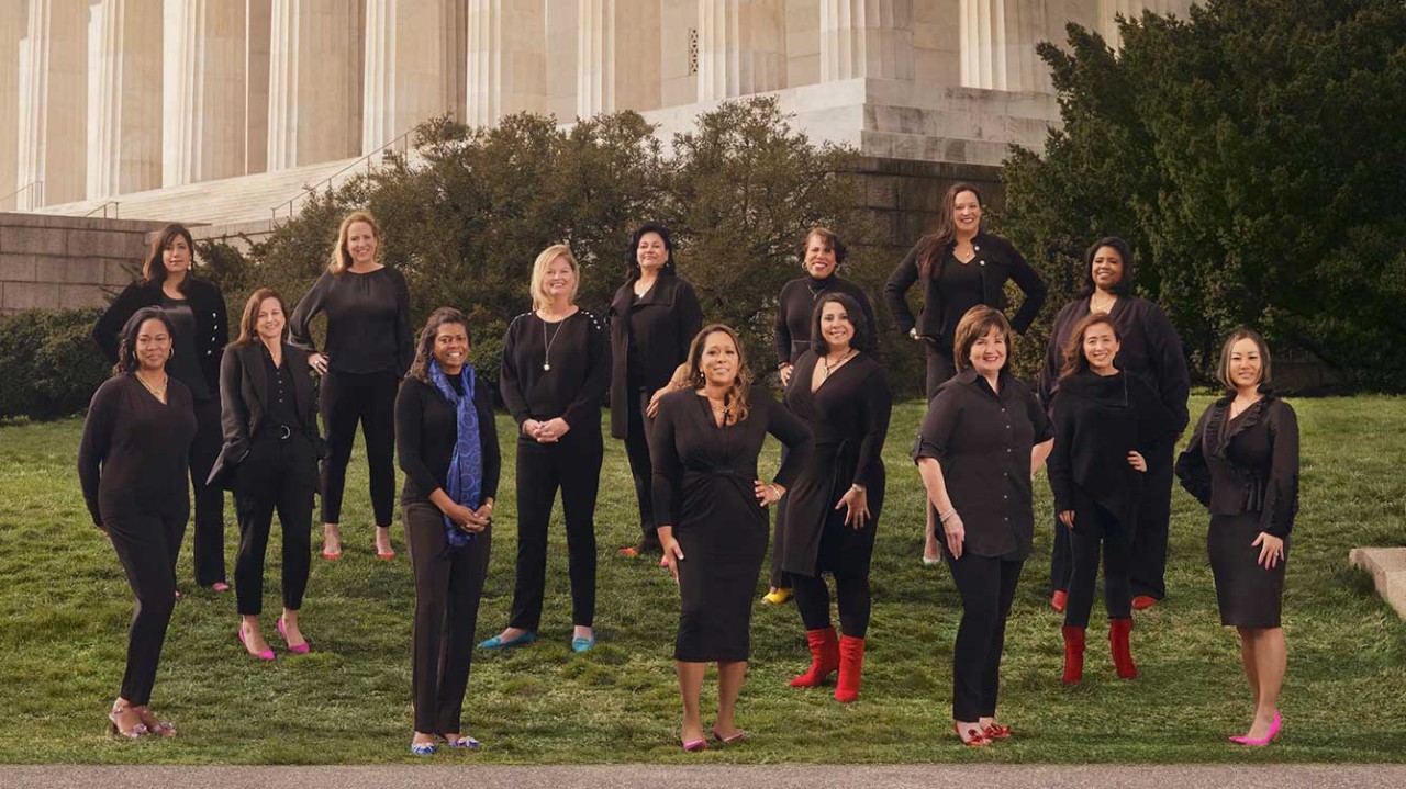 A large group of women in leadership at Booz Allen pose outside