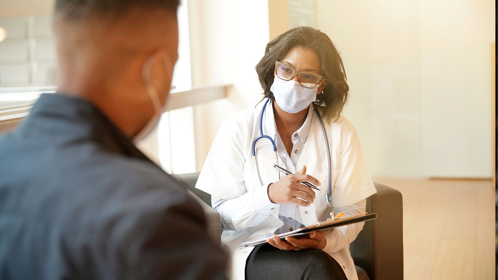 Female doctor discussing with patient holding clipboard.