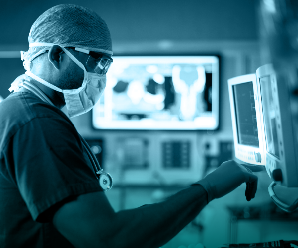 Doctor in goggles and a mask looking at patient data on computer monitors.