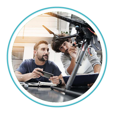 Male engineer sitting at a table with a phone on it examining security hardware, with another man standing next to him holding a screwdriver. 